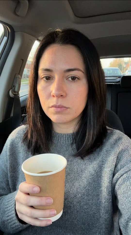 She stares into the phone, deadpan, coffee in hand.