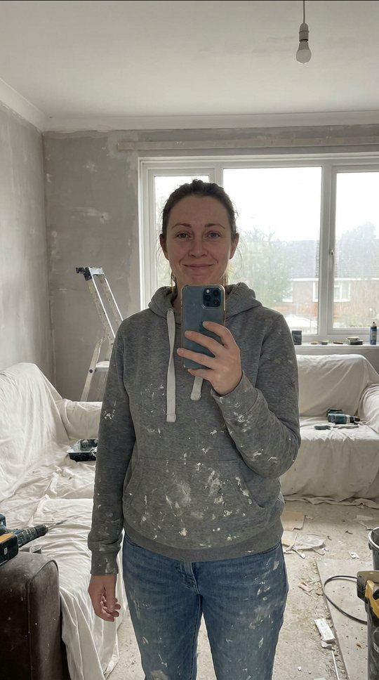 A half-stripped room, dust sheets, bare plaster. She holds up her phone.