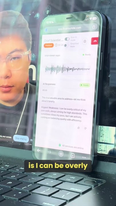 A laptop video interview with a phone propped in front of it generating the candidate's answer